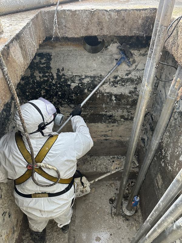 Operario con traje de protección y arnés limpiando una fosa industrial